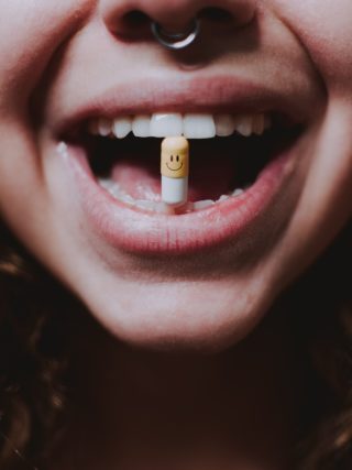 Laughing is the best medicine. Image of a woman holding between her teeth a pill with a smiley on it.